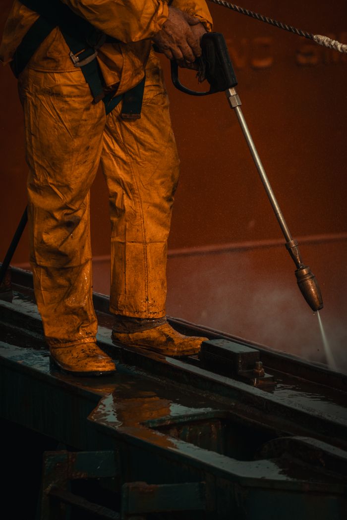 Un ouvrier équipé de protections jaunes nettoie du matériel industriel avec un nettoyeur à haute pression.