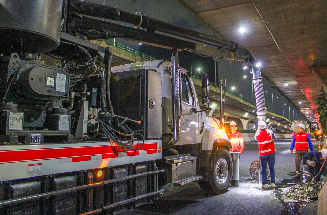 Workers cleaning streets with machinery under an overpass at night.